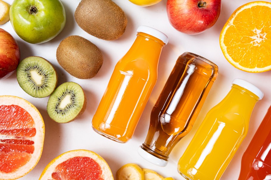 Verschiedene Fruchtsäfte in Glasflaschen neben Früchten wie Äpfeln, Kiwis und Orangen auf weißem Hintergrund