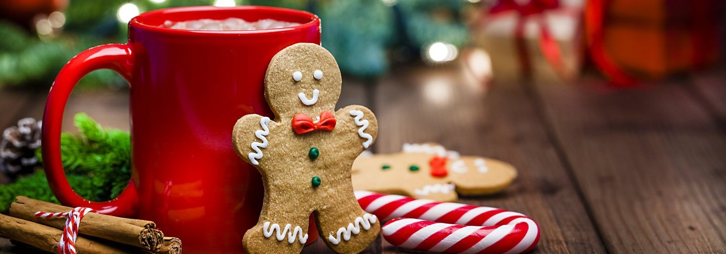 Lebkuchenmännchen, eine rote Tasse mit heißer Schokolade, eine Zuckerstange und Zimtstangen vor weihnachtlichem Hintergrund